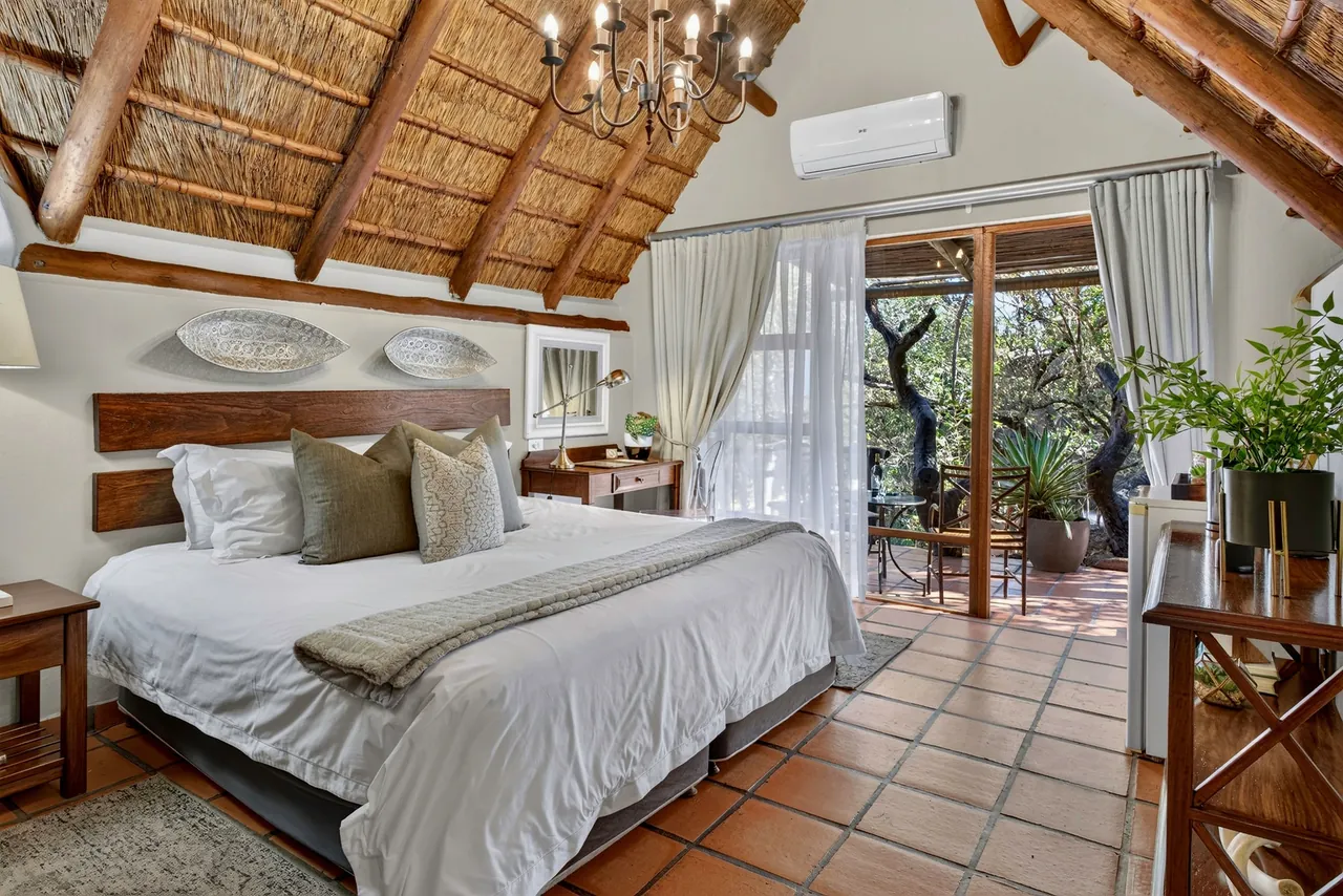Bedroom with a thatched ceiling and chandelier, doors open onto a private deck
