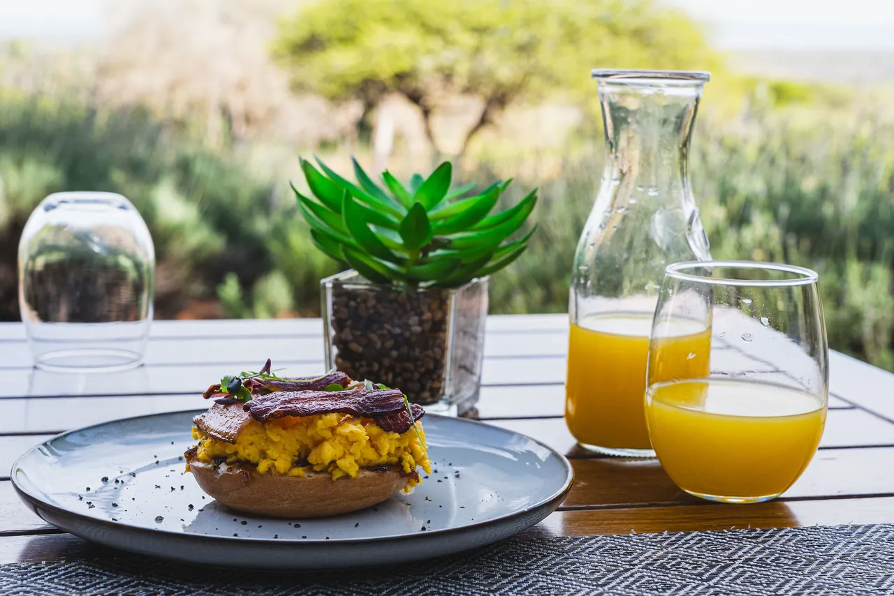 Plated breakfast with orange juice and a carafe, bushveld behind
