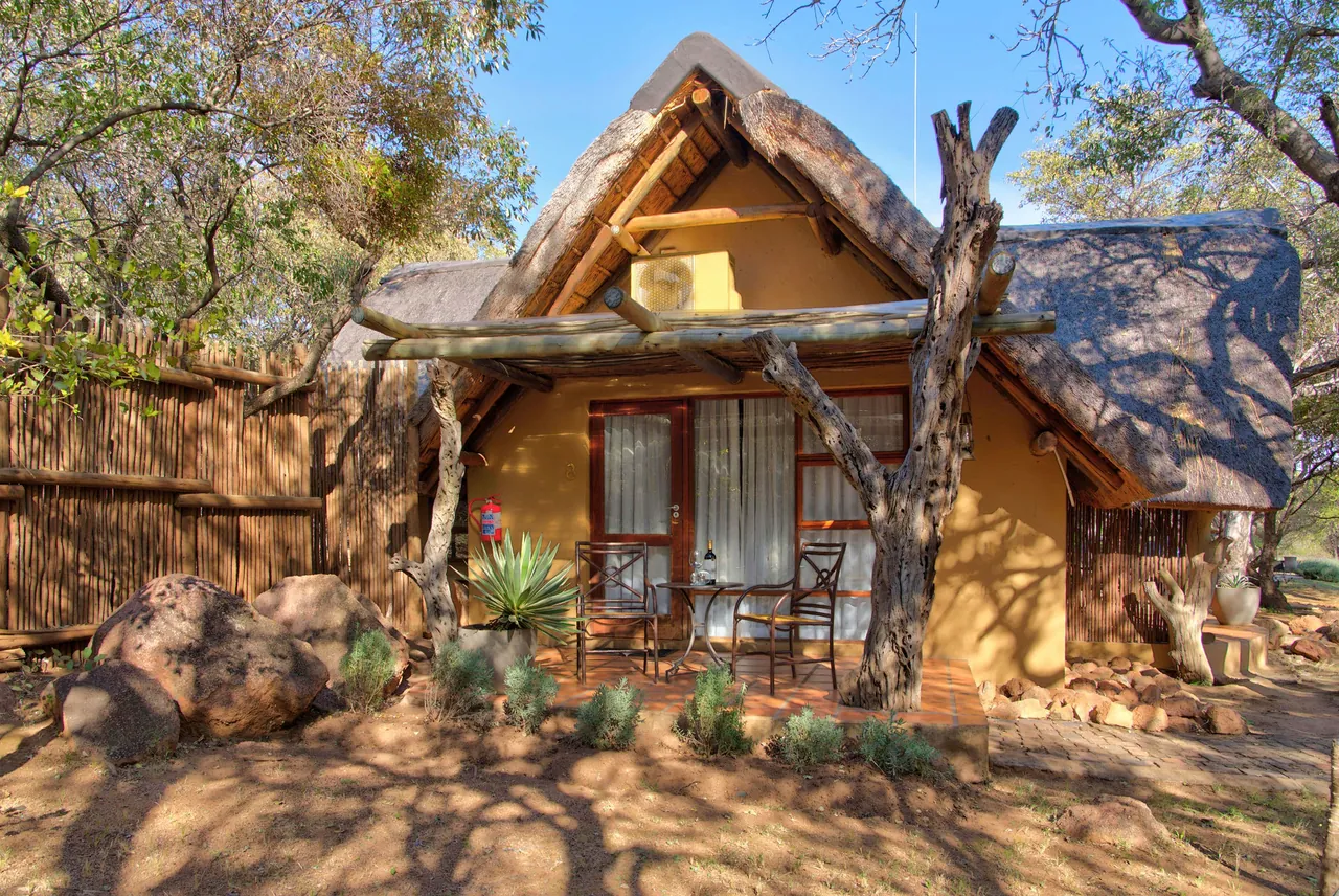 Thatched chalet with ochre walls and a timber veranda among trees