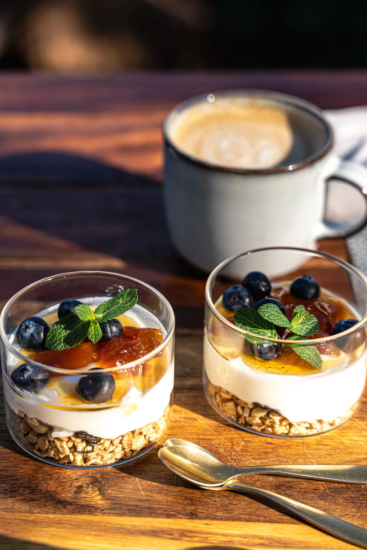 Two yoghurt parfaits with berries and a cup of coffee on a wooden table