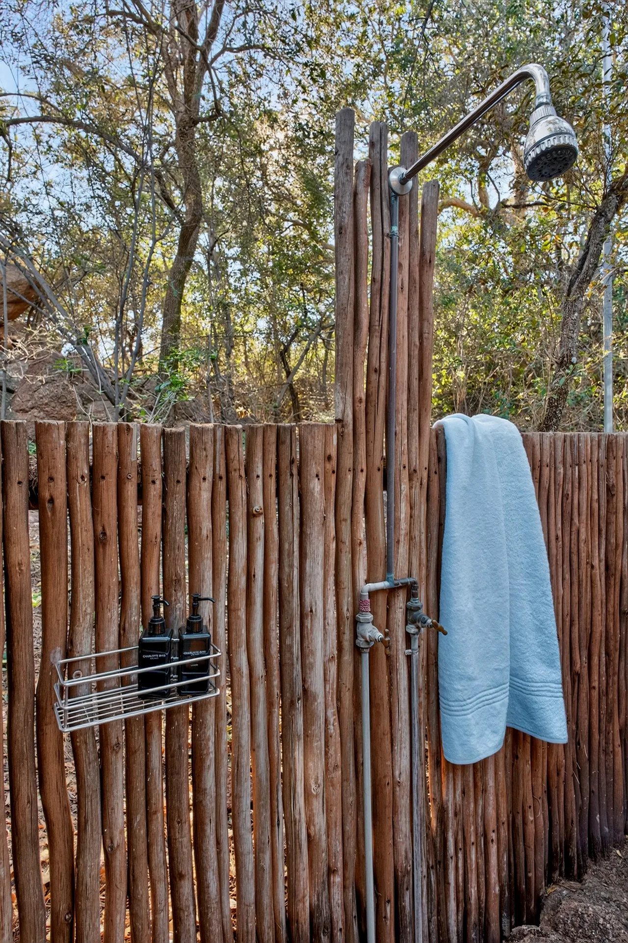 Outdoor shower behind a timber-pole screen with a blue towel