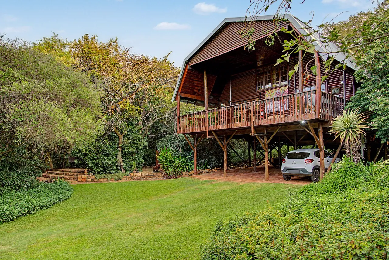 Raised timber chalet on stilts above a green lawn, surrounded by trees